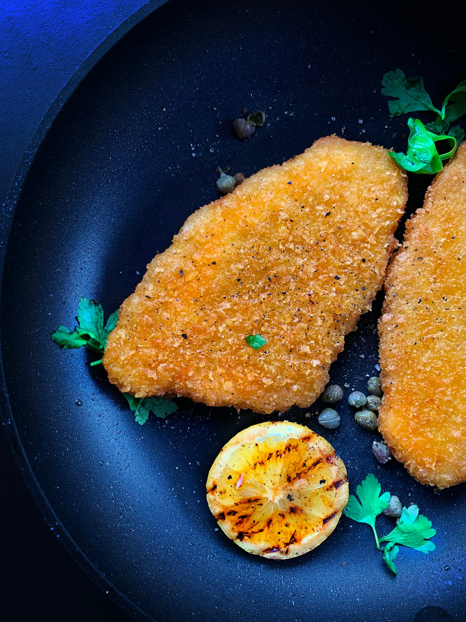 Two hand crumbed fillets on a deep blue pan with a charred lime